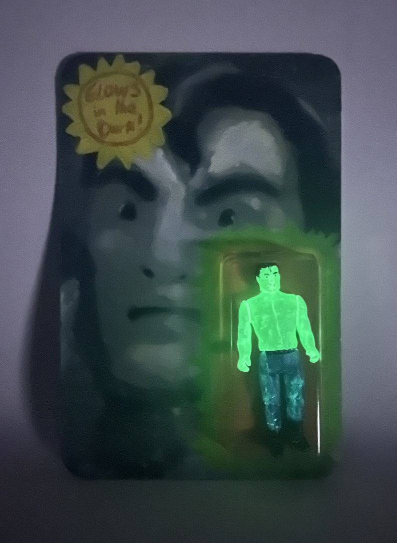 May include: A glow-in-the-dark action figure in a clear plastic package. The figure is a green humanoid with blue pants. The packaging features a painted face and the text "Glows in the Dark!" in a yellow sunburst.