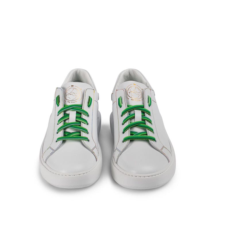 Puede incluir: Zapatillas bajas de cuero blanco con cordones verdes. Las zapatillas tienen una suela de goma blanca y un logotipo dorado en el lateral.