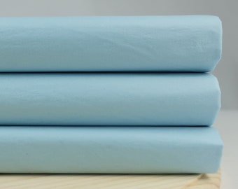 May include: Three rolls of light blue fabric stacked on top of each other on a wooden surface.