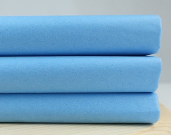 May include: Three rolls of light blue fabric stacked on top of each other on a wooden surface.