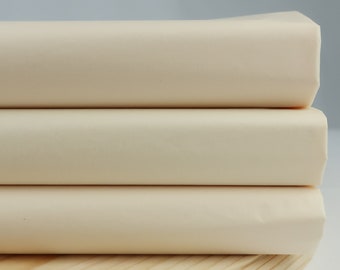 May include: Three rolls of off-white fabric stacked on top of a wooden surface.