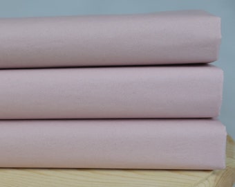May include: Three pieces of pale pink fabric stacked on top of each other on a wooden surface.