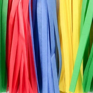 May include: A close-up of a colorful tissue paper streamer garland. The garland is made of green, red, blue, yellow, and green tissue paper streamers. The streamers are hanging down from a white background.