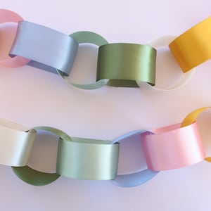 May include: A colorful paper chain garland with links in pastel shades of yellow, pink, blue, green, and white. The chain is arranged in a wavy pattern against a light background, suitable for party decorations.
