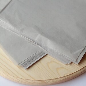 May include: A stack of gray tissue paper on a wooden round surface.