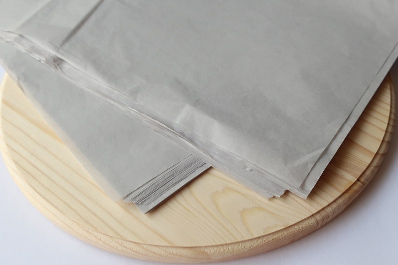 May include: A stack of gray tissue paper on a wooden round surface.