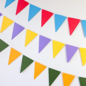 May include: A colorful paper banner with triangular flags in shades of yellow, orange, green, purple, blue and red. The banner is strung together with white string and is perfect for a party or celebration.