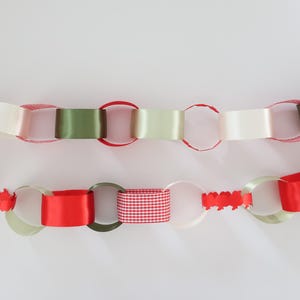 Op de afbeelding: Een decoratieve papieren kettingslinger met in elkaar grijpende lussen in verschillende texturen en kleuren, waaronder effen rood, olijfgroen, cr&egrave;me, rood-wit geblokte patronen en delen van rood papier die in kleine schulpranden zijn gesneden.