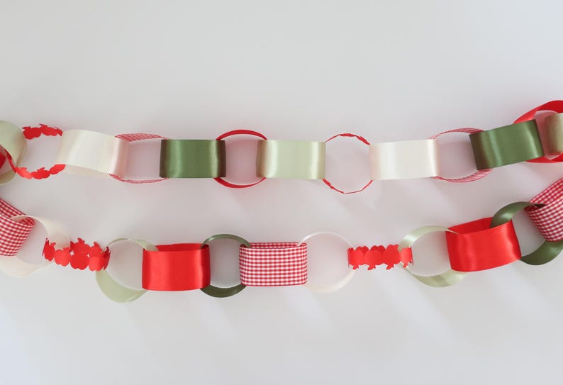 Op de afbeelding: Een decoratieve papieren kettingslinger met in elkaar grijpende lussen in verschillende texturen en kleuren, waaronder effen rood, olijfgroen, cr&egrave;me, rood-wit geblokte patronen en delen van rood papier die in kleine schulpranden zijn gesneden.