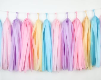 May include: A pastel colored tissue paper tassel garland with light blue, lavender, pink, and yellow tassels. The garland is strung on a white string and is perfect for a party or celebration.