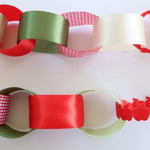 Op de afbeelding: Een decoratieve papieren kettingslinger met in elkaar grijpende lussen van diverse materialen. De schakels bestaan uit effen rode, olijfgroene en cr&egrave;mekleurige satijnen linten, rood-wit geblokt papier en rode papieren uitsparingen in de vorm van appels.