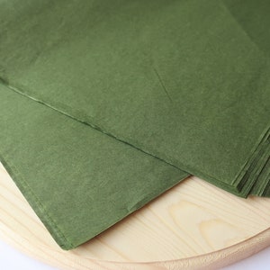 May include: A stack of green tissue paper on a wooden surface.