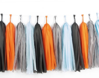 May include: A garland of tissue paper tassels in black, orange, and light blue. The tassels are strung together with white string.