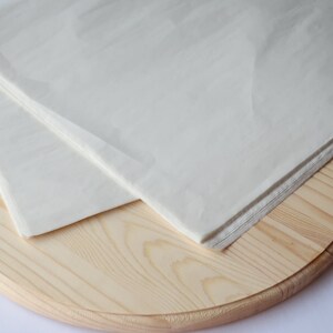May include: A white sheet of parchment paper folded in half and placed on a round wooden board.