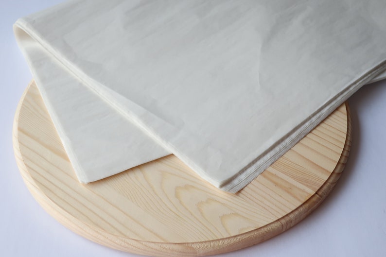 May include: A white sheet of parchment paper folded in half and placed on a round wooden board.
