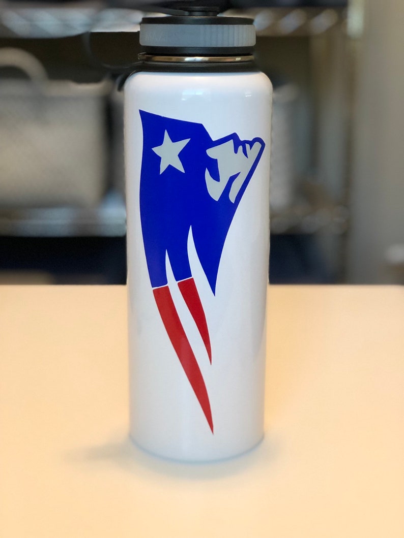 May include: White water bottle with a blue and red graphic design. The design features a blue shape with a white star and red accents. The bottle has a black and gray lid.