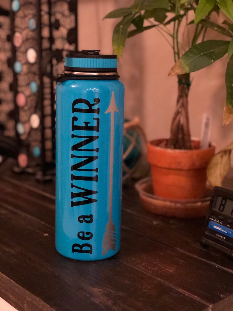 May include: A turquoise water bottle with a black lid and the words "Be a WINNER" in black, with a silver arrow design. The bottle is cylindrical and appears to be made of metal.