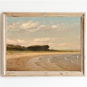 Op de afbeelding: Een ingelijst schilderij dat een zeezicht voorstelt met een zandstrand, blauw water en een rotsachtige uitstulping in de verte. De lucht is lichtblauw met pluizige witte wolken.