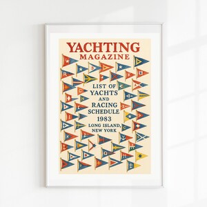 May include: Framed vintage "Yachting Magazine" poster. The poster features a cream background with red, blue, and yellow pennant flags. Text includes "YACHTING MAGAZINE", "LIST OF YACHTS AND RACING SCHEDULE 1983", and "LONG ISLAND, NEW YORK".