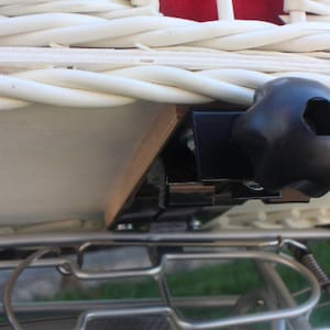 Puede incluir: Primer plano de una cesta de bicicleta de mimbre blanca con interior rojo. La cesta est&aacute; montada en un portaequipajes de bicicleta con un soporte de montaje negro. La cesta est&aacute; dise&ntilde;ada para transportar objetos en bicicleta.