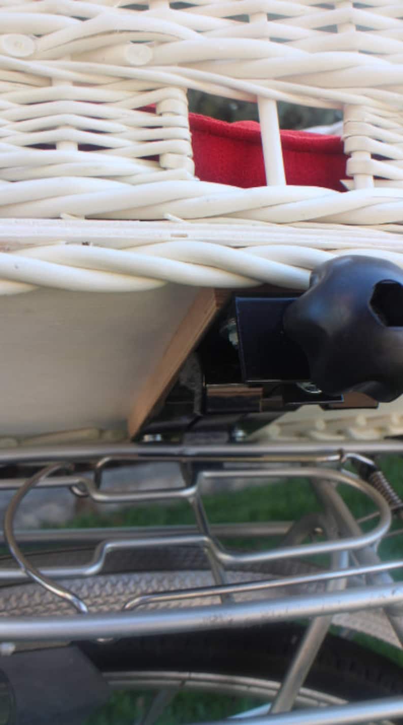 Puede incluir: Primer plano de una cesta de bicicleta de mimbre blanca con interior rojo. La cesta est&aacute; montada en un portaequipajes de bicicleta con un soporte de montaje negro. La cesta est&aacute; dise&ntilde;ada para transportar objetos en bicicleta.