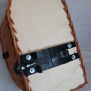 Puede incluir: Una cesta de mimbre para bicicleta con una base de madera de color claro. La cesta tiene un exterior tejido marr&oacute;n y un soporte de montaje de metal negro con pernos. La cesta est&aacute; dise&ntilde;ada para sujetarse a una bicicleta.