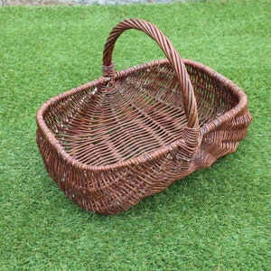 May include: A brown wicker basket with a handle. The basket is empty and sitting on a green grassy surface.