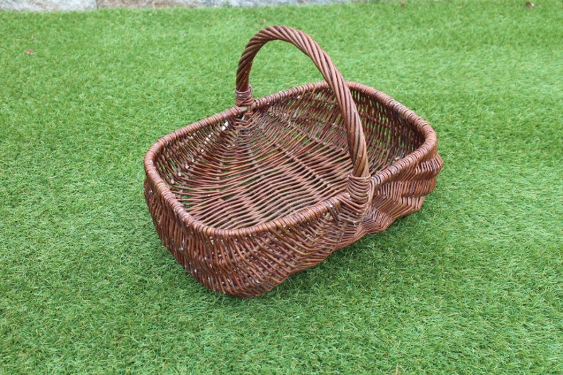 May include: A brown wicker basket with a handle. The basket is empty and sitting on a green grassy surface.