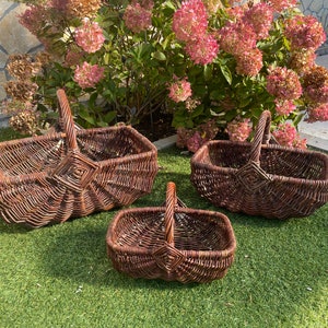 May include: Three brown wicker baskets of varying sizes with handles. The baskets are arranged on a green grassy surface.