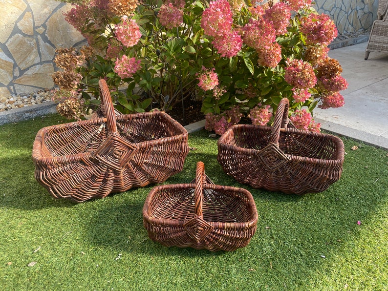 May include: Three brown wicker baskets of varying sizes with handles. The baskets are arranged on a green grassy surface.