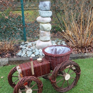 May include: A wicker planter shaped like a tractor with a brown wicker pot on top. The planter is sitting on green grass.