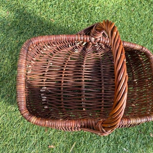 May include: A brown wicker basket with a single handle. The basket is woven with a tight, even pattern.