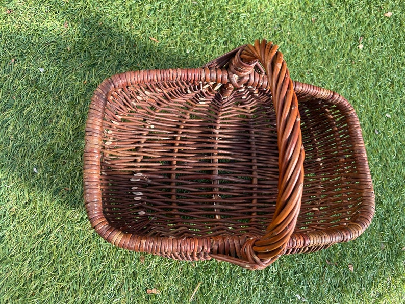 May include: A brown wicker basket with a single handle. The basket is woven with a tight, even pattern.