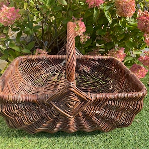 May include: A brown wicker basket with a woven handle. The basket is sitting on a green grassy surface.