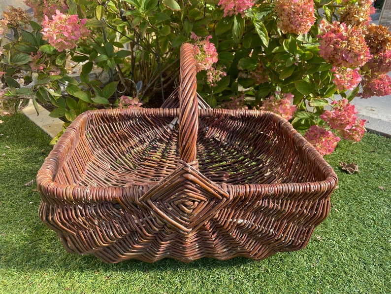 May include: A brown wicker basket with a woven handle. The basket is sitting on a green grassy surface.