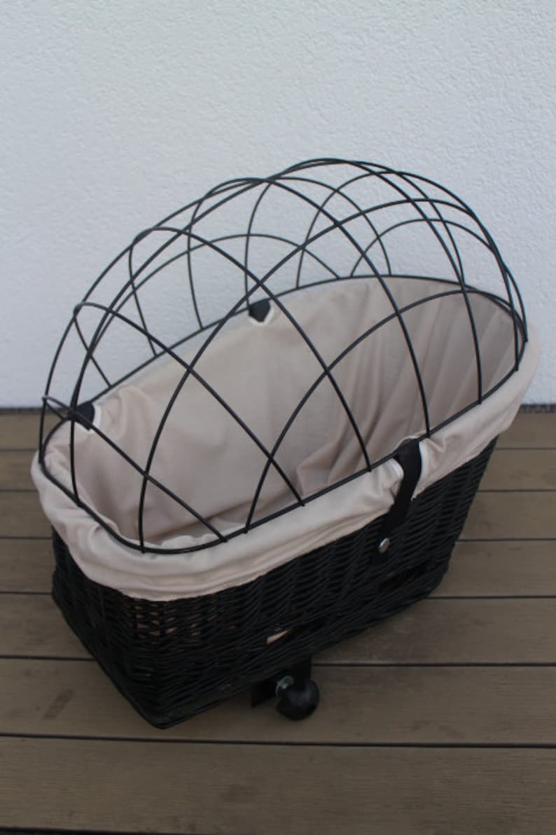 Puede incluir: Cesta de bicicleta de mimbre negro con una parte superior de jaula de alambre negro y un forro de tela beige. La cesta tiene una forma redondeada y est&aacute; dise&ntilde;ada para sujetarse a una bicicleta. La cesta tiene una peque&ntilde;a rueda en la parte inferior.