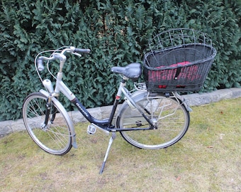 Puede incluir: Una bicicleta plateada con una cesta negra en la parte trasera. La cesta está hecha de mimbre y tiene un marco de metal negro. La bicicleta tiene un asiento negro y un manillar negro.