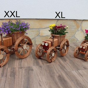 May include: Three wicker planter tractors in different sizes, labeled XXL, XL, and L. The XXL tractor is brown with purple flowers, the XL tractor is brown with yellow flowers, and the L tractor is brown with pink flowers.
