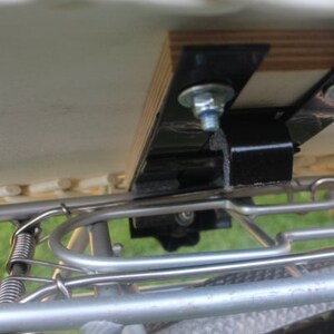 Puede incluir: Primer plano de un accesorio para portaequipajes de bicicleta. El portaequipajes es de metal plateado y tiene una base de madera. Los soportes y pernos de metal negro aseguran el portaequipajes al cuadro de la bicicleta.