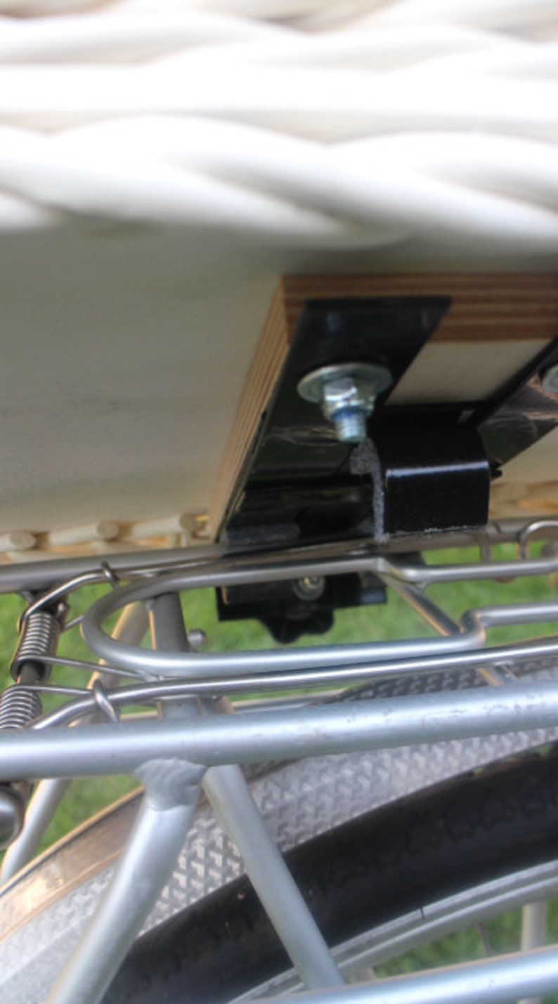 Puede incluir: Primer plano de un accesorio para portaequipajes de bicicleta. El portaequipajes es de metal plateado y tiene una base de madera. Los soportes y pernos de metal negro aseguran el portaequipajes al cuadro de la bicicleta.