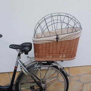 Op de afbeelding: Een zwarte fiets met een rieten mand en een metalen kooi aan de achterkant. De mand is gevoerd met een beige stof.