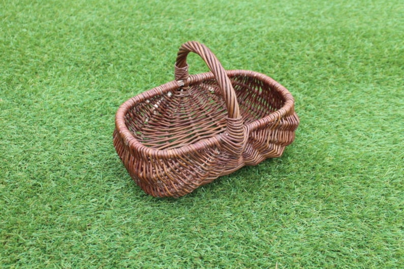 May include: A brown wicker basket with a handle. The basket is oval shaped and has a woven pattern.