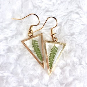 May include: A pair of gold triangle earrings with a pressed green fern leaf inside each triangle.