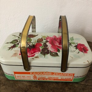 Könnte beinhalten: Eine vintage Metalldose mit goldenen Griffen und einem Blumendesign. Die Dose ist mit "Kaugummi-Zigarren" und "Ganz Grosse Klasse" sowie dem Markennamen "Wiko" beschriftet. Die Dose enthält 200 Stück.