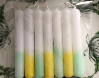 Könnte beinhalten: Ein Set mit acht weißen Stumpenkerzen mit einem grünen und gelben Ombre-Effekt. Die Kerzen sind in einer durchsichtigen Plastiktüte verpackt.