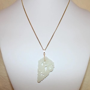 May include: A white jade pendant necklace with a delicate gold chain. The pendant is carved with a floral design and has a slightly translucent appearance.