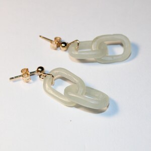 May include: A pair of gold-toned chain link earrings with a pale green, translucent appearance. The earrings have a post-and-ball closure. The chain links are oval-shaped and connected to each other.