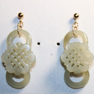 May include: A pair of jade earrings with a gold post and a carved flower design. The earrings are in the shape of a circle with a flower in the center.