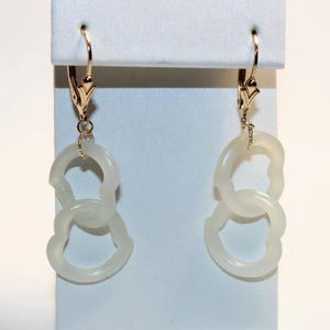May include: A pair of white jade earrings with a gold-tone hook closure. The earrings are shaped like two interlocking circles.