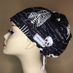 May include: A black surgical scrub cap with a white anatomical skeleton print. The cap features a skull, rib cage, and bone diagrams. The text "The Human Body" and "ANIAMADETHIS" are visible.